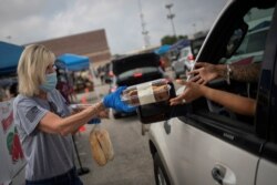 FILE - Volunteer Cindy Trevino hands bread and pastries to a resident, affected by the economic fallout caused by the coronavirus disease (COVID-19) pandemic, during a San Antonio Food Bank distribution in San Antonio, Texas, July 17, 2020.