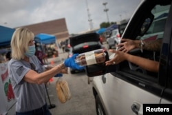 FILE - Volunteer Cindy Trevino hands bread and pastries to a resident, affected by the economic fallout caused by the coronavirus disease (COVID-19) pandemic, during a San Antonio Food Bank distribution in San Antonio, Texas, July 17, 2020.