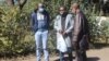 Journalists Samuel Takawira and Frank Chikowore stand with a police detective outside a court in Harare, Zimbabwe, May 23, 2020. (Columbus Mavhunga/VOA) 