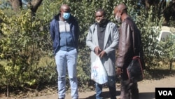 Journalists Samuel Takawira and Frank Chikowore stand with a police detective outside a court in Harare, Zimbabwe, May 23, 2020. (Columbus Mavhunga/VOA) 