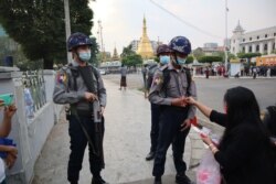 A woman offers a face mask to a police officer during a protest against the military coup near the Sule Pagoda in Yangon, Myanmar, Feb. 7, 2021. (VOA Burmese Service)