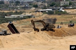 FILE - A backhoe removes sand barriers to create a buffer zone along the Egyptian border with the Gaza strip, near entrances to smuggling tunnels, background, in Rafah, June 28, 2017.