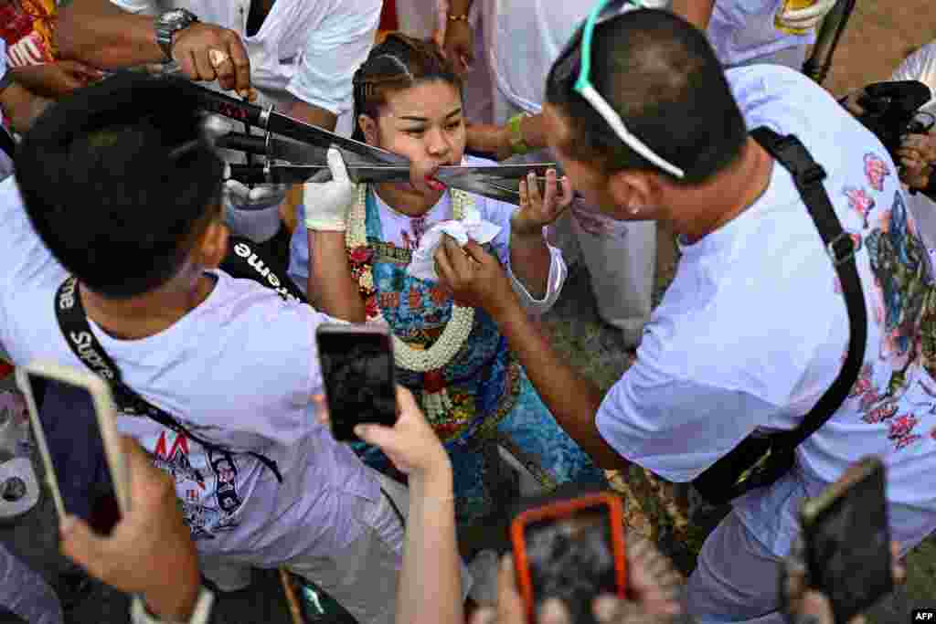 Sirinnicha Thampradit, a devotee of the Jor Soo Gong Naka shrine, has swords pierced through her cheek as she takes part in a procession during the vegetarian festival in Phuket.