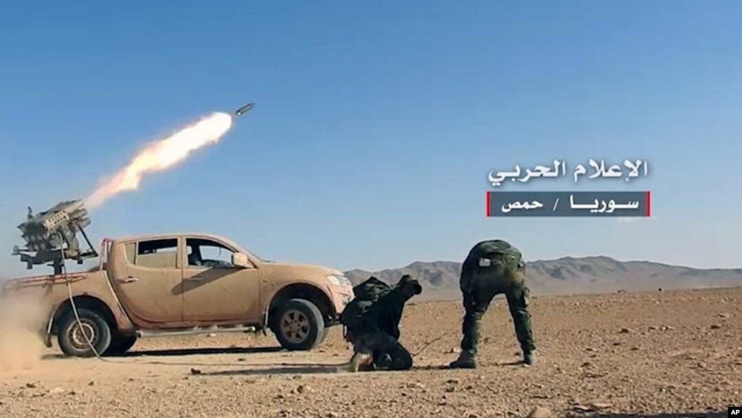 This May 25, 2017 photo provided by the government-controlled Syrian Central Military Media, shows Syrian government troops firing multiple launcher rockets at insurgent group's position in the Syrian province of Homs. 
