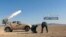 This May 25, 2017 photo provided by the government-controlled Syrian Central Military Media, shows Syrian government troops firing multiple launcher rockets at insurgent group's position in the Syrian province of Homs. 