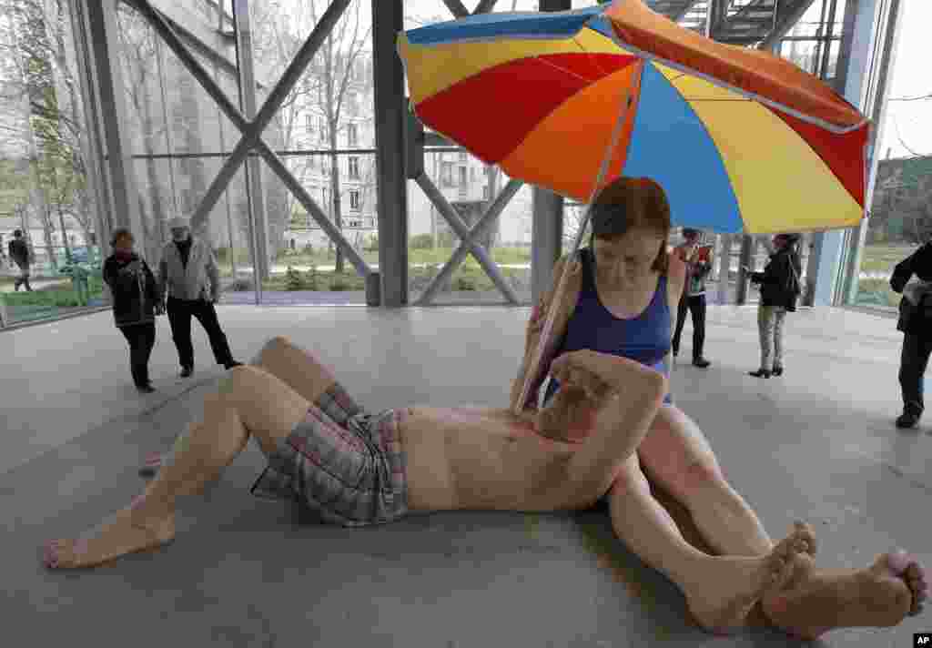 Visitors look at a sculpture entitled "Couple Under an Umbrella, 2013" by Australian artist Ron Mueck during the opening day for his exhibition at the Fondation Cartier pour l'Art Contemporain in Paris.