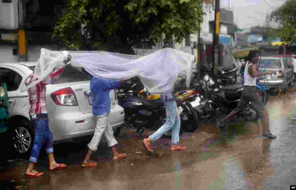 Tiga orang laki-laki India menutupi diri mereka dengan lembaran plastik agar tidak kehujanan di New Delhi, India. Musim hujan yang biasanya turun di India dari bulan Juni hingga September sangat penting bagi para petani di negara itu&nbsp; yang hasil panennya digunakan untuk memenuhi kebutuhan pangan ratusan juta orang.