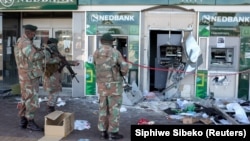 Des militaires inspectent des distributeurs automatiques de billets endommagés à l'extérieur d'une banque à Soweto, en Afrique du Sud, le 13 juillet 2021. 