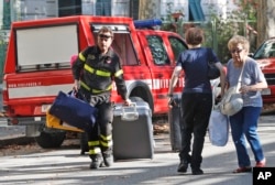 A firefighter pulls a suitcase and carries bags as he accompanies residents to get their belongings from their homes, in Genoa, Italy, Aug. 16, 2018.
