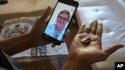 FILE - Public health nurse Peggy Cooley of the Tacoma-Pierce County Health Department, seen on the phone screen, uses Skype video to remotely monitor a patient taking antibiotics for tuberculosis at home in Lakewood, Wash, March 15, 2018. 