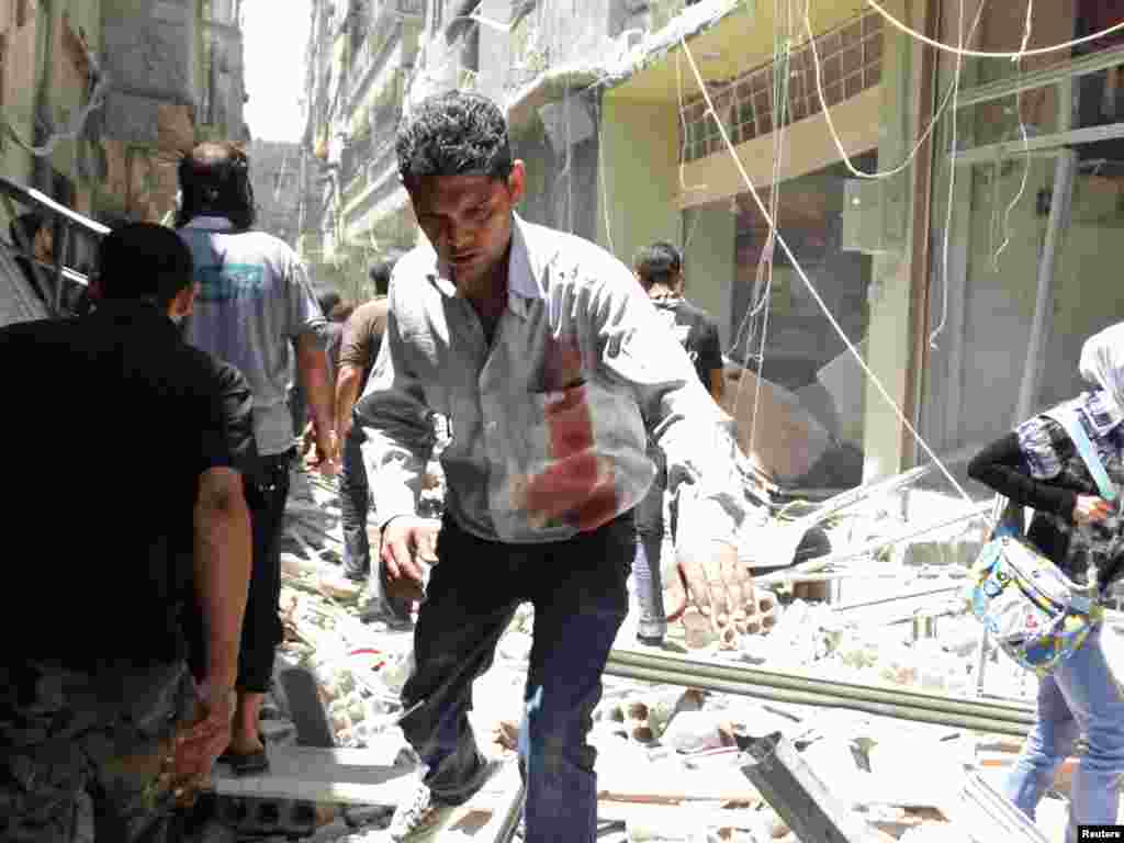 A man with bloodstains on his shirt walks on rubble after what activists said was an airstrike by forces loyal to Syria's President Bashar al-Assad at the Damascus suburb of Saqba, June 18, 2014.