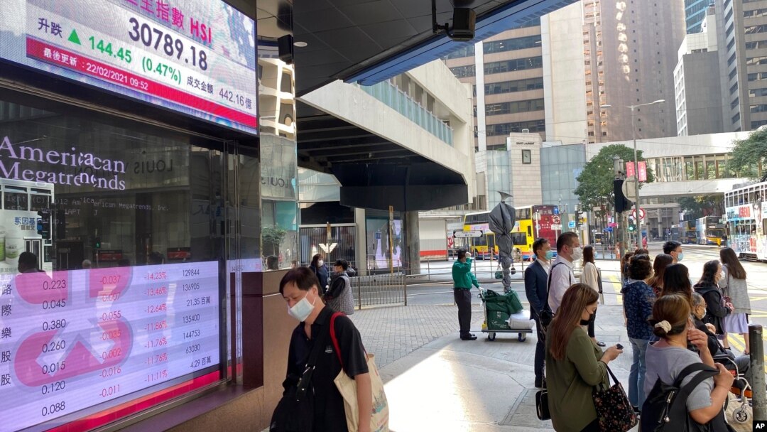 2021年2月22日人们走过显示香港股票指数的银行电子板。