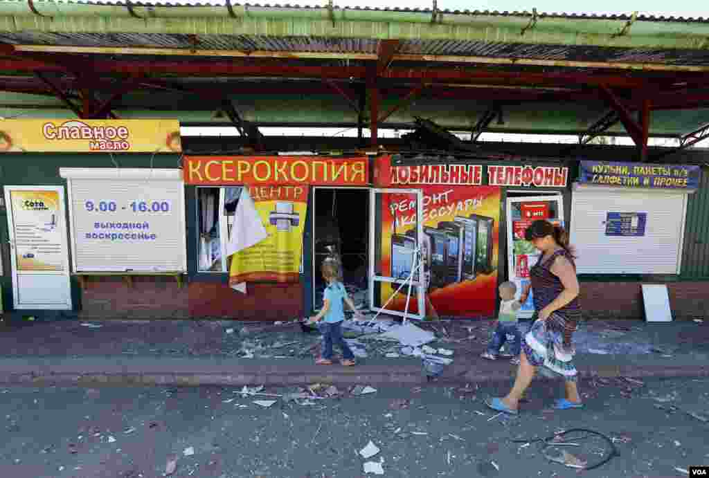 Seorang perempuan dan anak-anak berjalan melewati jalanan pasar yang rusak di Slovyansk, Ukraina Timur (1/7).