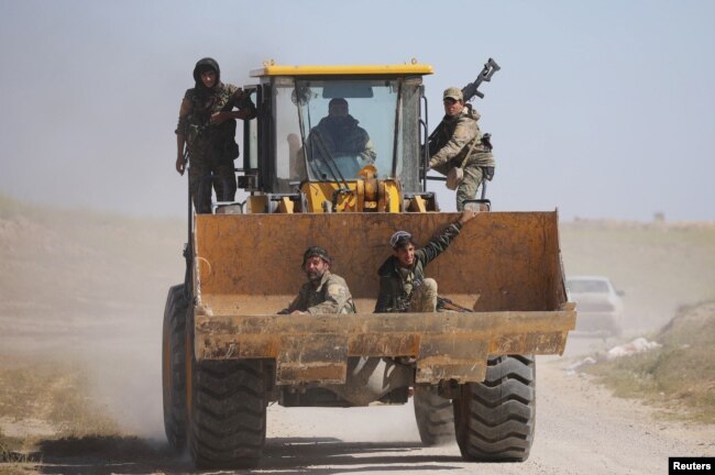 Fighters from the Syrian Democratic Forces sit in the bucket of an excavator in the village of Baghuz, Deir el-Zour province, Syria, March 20, 2019.