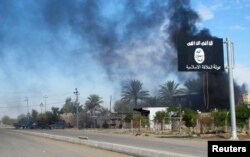 FILE - Smoke raises behind an Islamic State flag in Iraq, Nov. 24, 2014.