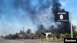 FILE - Smoke raises behind an Islamic State flag flying in Diyala province, Iraq, Nov. 24, 2014.