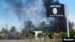 FILE - Smoke raises behind an Islamic State flag in Diyala province, Iraq, Nov. 24, 2014.
