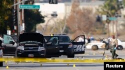 Un policier ramasse une arme près du véhicule à bord duquel était le couple des auteurs présumés de la fusillade de San Bernardino qui ont été abattus, en Californie, 3 décembre 2015.