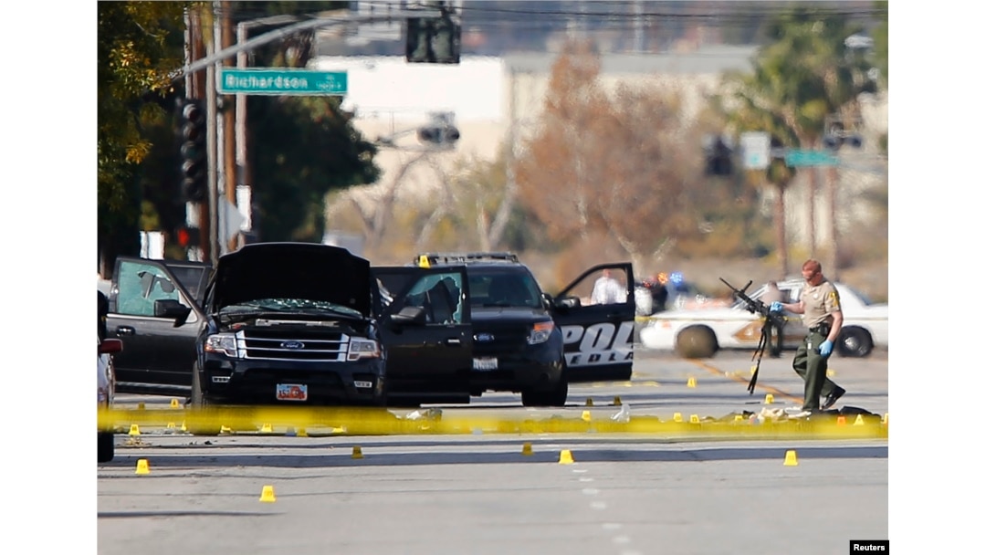 FILE - A police officer picks up a weapon from the scene of the investigation around the area of the SUV vehicle where two suspects were shot by police following a mass shooting in San Bernardino, California, Dec. 3, 2015.