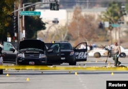 FILE - A police officer picks up a weapon from the scene of the investigation around the area of the SUV vehicle where two suspects were shot by police following a mass shooting in San Bernardino, California, Dec. 3, 2015.