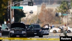 12月3日在加州圣贝纳迪诺枪击案嫌疑人的休旅车调查现场附近，一名警察拿起一把武器。这次大规模枪击案的两名嫌疑人被警方开枪打死。