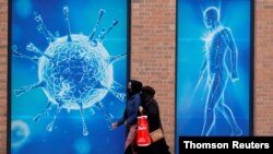 People walk past an illustration of a virus in Oldham, Britain Aug. 3, 2020.