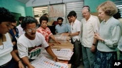 ARCHIVO - El expresidente de EEUU Jimmy Carter y su esposa Rosalynn, derecha, observan mientras trabajadores electorales preparan boletas en un centro de votación en Managua, Nicaragua, el 25 de febrero de 1990. Los Carter fueron a Nicaragua como observadores electorales.