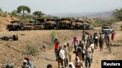 FILE - Villagers return from a market to Yechila town in south central Tigray walking past scores of burned vehicles, in Tigray, Ethiopia, July 10, 2021.