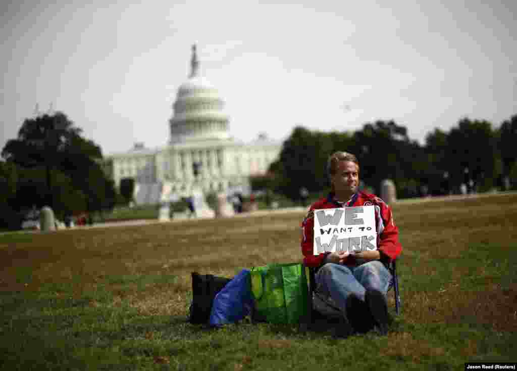 Um funcionário do governo que foi despedido temporariamente senta-se sozinho na esplanada de Washington com ur cartaz que diz  "Queremos trabalhar"