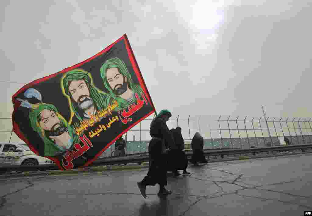 A Shiite Muslim pilgrim carries a flag depicting the Prophet Mohammed&#39;s cousin Ali ibn Abi Taleb and his two sons on the outskirts of Baghdad on the way to the holy Iraqi city of Karbala.