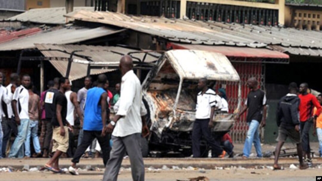 Residents look at a vehicle of FDS - troops loyal to incumbent president Laurent Gbagbo - burned in the Abobo district of Abidjan, 12 Jan 2011