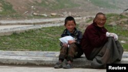 Người đàn ông và một cậu bé Tây Tạng ngồi gần Tu viện Jonang Dzamthang. Trung Quốc nhấn mạnh rằng các vụ dời cư là hoàn toàn trên căn bản tự nguyện và người dân Tây Tạng biết ơn vì có được nhà mới.