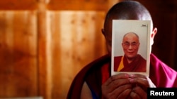 FILE - A monk holds a picture of Tibetan spiritual leader Dalai Lama inside of his room at Labrang Monastery in Xiahe county, Gansu Province Feb. 21, 2012.