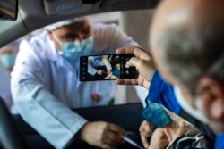 A man photographs his mother getting a shot of China's Sinovac CoronaVac vaccine for COVID-19 during a priority vaccination program for the elderly at a drive-thru site in the Pacaembu soccer stadium parking lot in Sao Paulo, Brazil, Feb. 8, 2021.