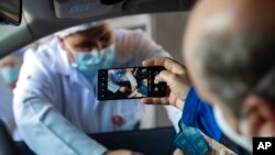 FILE - A man photographs his mother getting a shot of a COVID-19 vaccine during a priority vaccination program for the elderly at a drive-through site set up at the Pacaembu soccer stadium parkinglot in Sao Paulo, Brazil, Feb. 8, 2021.