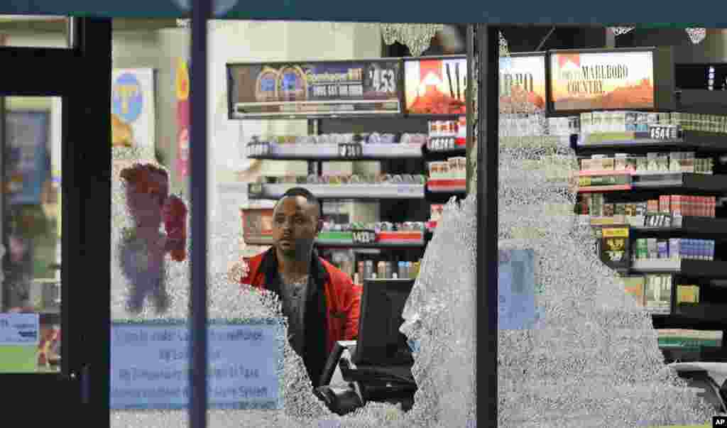 A clerk looks at broke windows shot out at a store in downtown Dallas, Friday, July 8, 2016.
