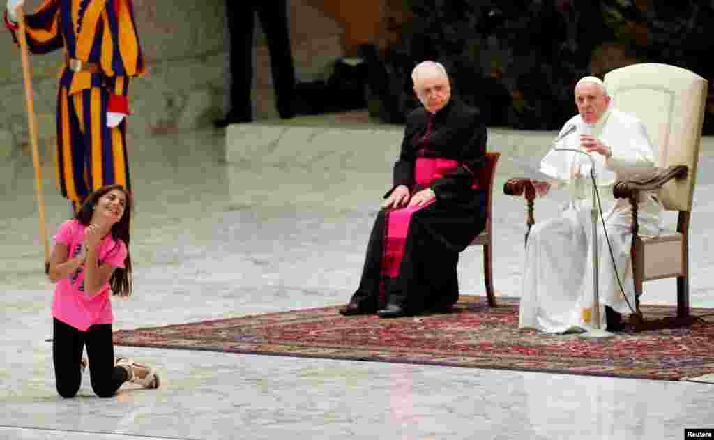 Pope Francis lets a little girl suffering from an illness to move around, clapping and dancing on the stage, for most of his general audience in Paul VI Hall at the Vatican.