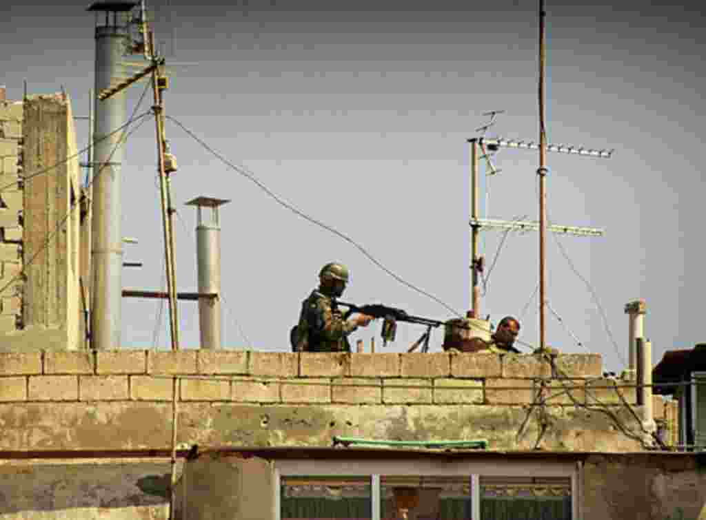 In this undated citizen journalism image made on a mobile phone and acquired by the AP, Syrian soldiers stand on the roof of a building in an undisclosed location in Syria