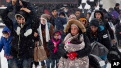 FILE - A group of migrants move through snow toward a train station to be transferred to Austria, near the border with Croatia, in Dobova, Slovenia, Jan. 3, 2016.