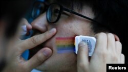 Seorang peserta memulas cat warna pelangi di wajah rekannya sebelum mulai acara lari bersama untuk memperingati Hari Internasional Melawan Homophobia di sebuah taman di Beijing, China, 17 Mei 2018.