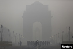 A man rides his bicycle next to Indian soldiers marching in front of India Gate on a smoggy morning in New Delhi, India, December 1, 2015.