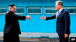 El líder de Corea del Norte, Kim Jong Un, a la izquierda, y el presidente de Corea del Sur, Moon Jae-in, extienden sus manos para saludarse en la Zona Desmilitarizada que separa sus naciones. Abril 27, 2018. 