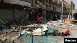 Residents stand amid debris near shops damaged by a car bomb attack that occurred late on Monday in east of Baghdad, Iraq, July 24, 2012. 