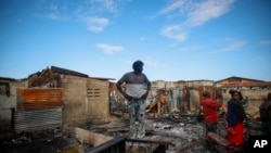 Residents stand amid houses damaged when a gasoline truck overturned and exploded in Cap-Hatien, Haiti, Dec. 14, 2021.