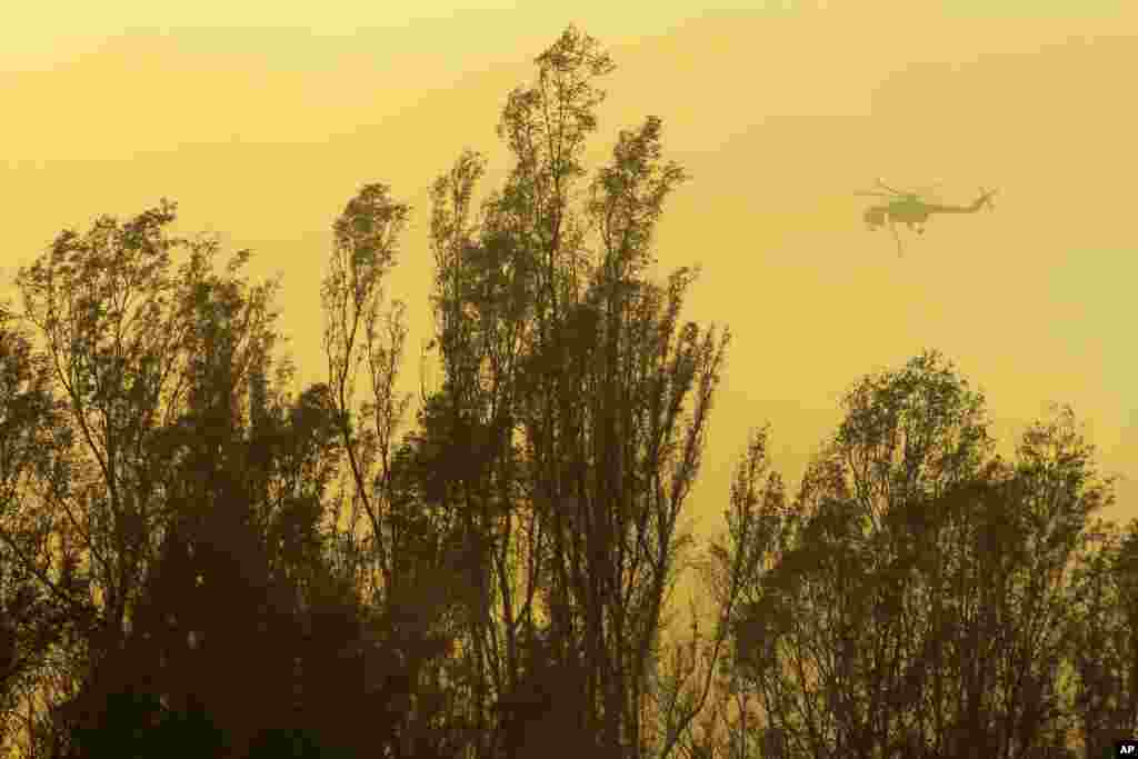 A helicopter transporting water flies over trees during a wildfire in Escondido, California, May 15, 2014.