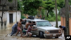 Residentes trabajan juntos para empujar un vehículo atascado en una calle inundada por el paso del huracán John, en Acapulco, México, el 27 de septiembre de 2024.