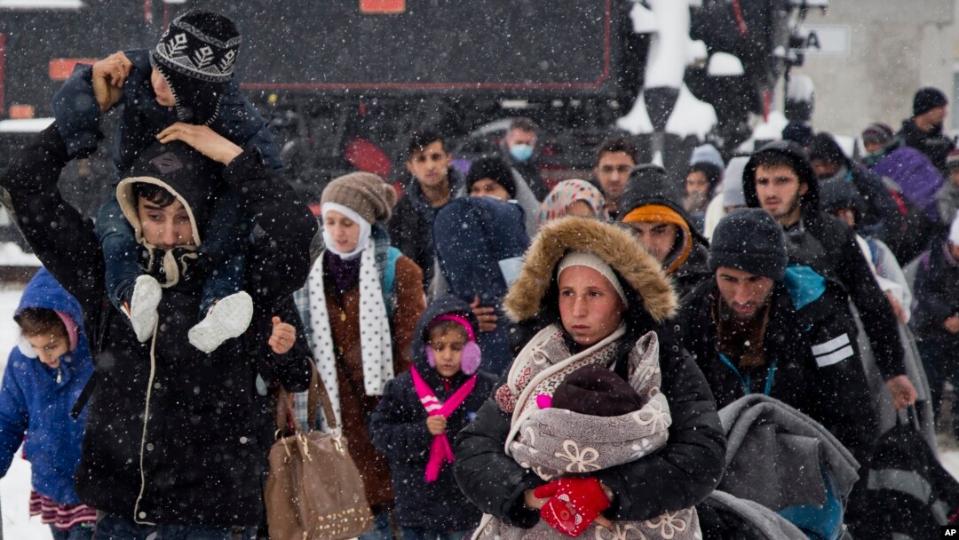 FILE - A group of migrants moves through snow toward a train station to be transferred to Austria, near the border with Croatia, in Dobova, Slovenia, Jan. 3, 2016.