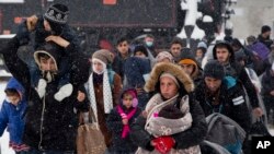 FILE - A group of migrants moves through snow toward a train station to be transferred to Austria, near the border with Croatia, in Dobova, Slovenia, Jan. 3, 2016.