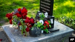 FILE —Flowers and a helmet rest at the memorial stone that commemorates the death of six Ukrainian soldiers killed by Russians, in the yard of the Church of the Intercession of the Blessed Virgin Mary in, Lypivka, near Lviv, Ukraine, April 28, 2024