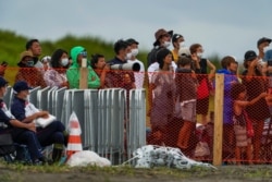 People watch from behind a security fence during the final day of the surfing competition at the 2020 Summer Olympics, July 27, 2021, at Tsurigasaki beach in Ichinomiya, Japan.